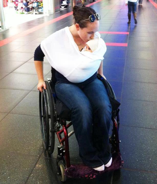 Mere en fauteuil roulant portant son enfant dans un harnais